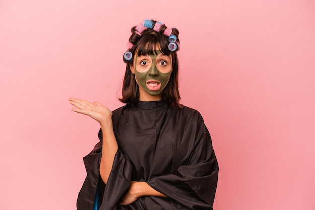 Young mixed race woman waiting in a Beaty salon isolated on pink background showing a copy space on a palm and holding another hand on waist