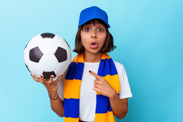 Young mixed race woman watching soccer isolated on blue background pointing to the side