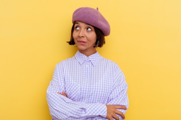 目標と目的を達成することを夢見て黄色の壁に分離されたベレー帽を身に着けている若い混血の女性