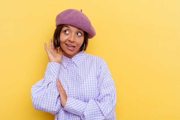 Young mixed race woman wearing a beret isolated on yellow wall trying to listening a gossip.