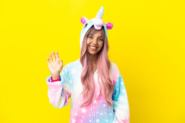 Young mixed race woman wearing a unicorn pajama isolated on white background saluting with hand with happy expression