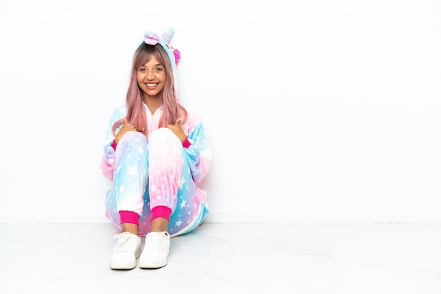 Young mixed race woman wearing a unicorn pajama sitting on the floor isolated on white background with surprise facial expression