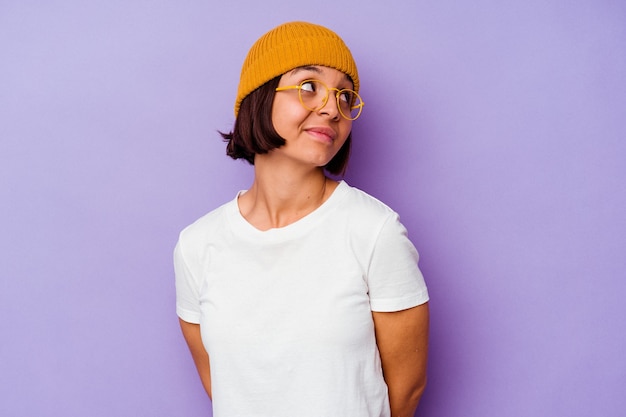 Young mixed race woman wearing a wool cap isolated on purple background dreaming of achieving goals and purposes