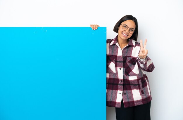 Young mixed race woman with a big blue placard isolated smiling and showing victory sign