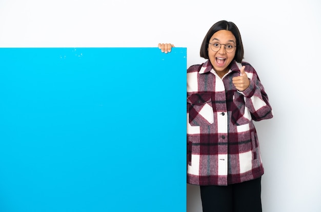 Молодая женщина смешанной расы с большим синим плакатом, изолированным на белом фоне, показывает знак ОК и жест пальца вверх