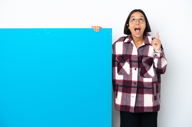Молодая женщина смешанной расы с большим синим плакатом на белом фоне удивлена и указывает вверх