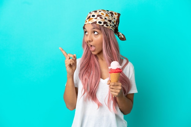 Young mixed race woman with a cornet ice cream isolated on blue background intending to realizes the solution while lifting a finger up