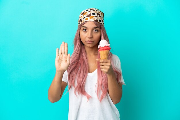 Young mixed race woman with a cornet ice cream isolated on blue background making stop gesture