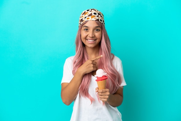 Young mixed race woman with a cornet ice cream isolated on blue background pointing to the side to present a product