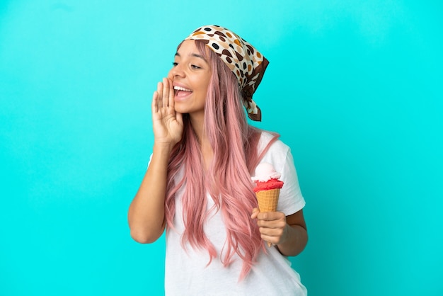 Photo young mixed race woman with a cornet ice cream isolated on blue background shouting with mouth wide open to the side