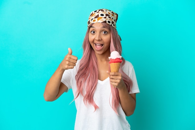 Young mixed race woman with a cornet ice cream isolated on blue background with thumbs up because something good has happened