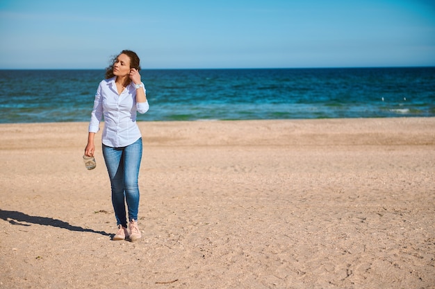 Young mixed race woman with curly hair walking on the beach on a sunny day