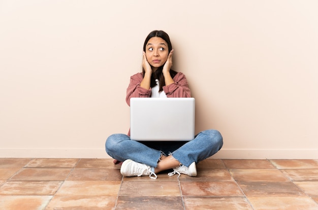 Young mixed race woman with a laptop sitting on the floor frustrated