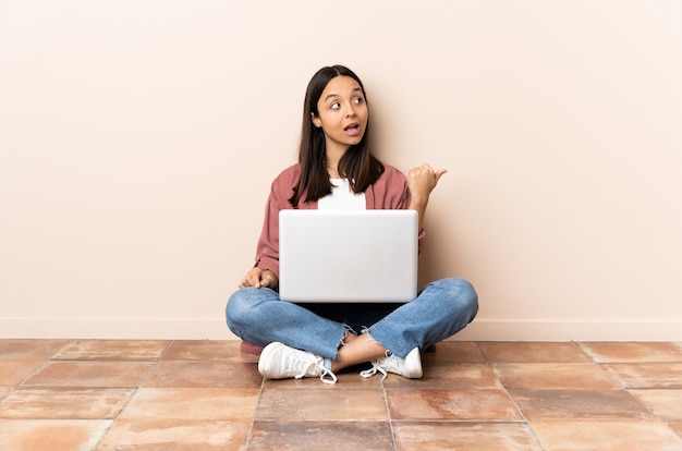 Young mixed race woman with a laptop sitting on the floor