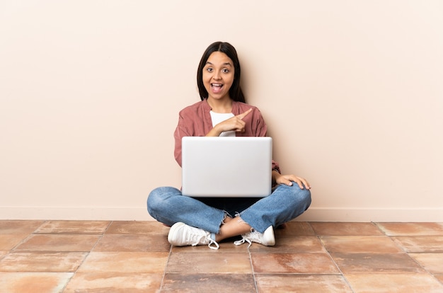 Young mixed race woman with a laptop sitting on the floor