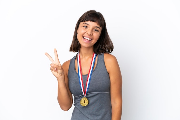 Young mixed race woman with medals isolated on white background smiling and showing victory sign