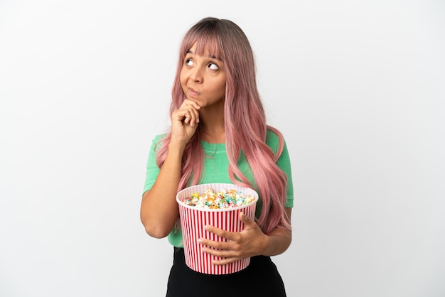 白い背景で隔離のポップコーンを食べて見上げるピンクの髪を持つ若い混血の女性