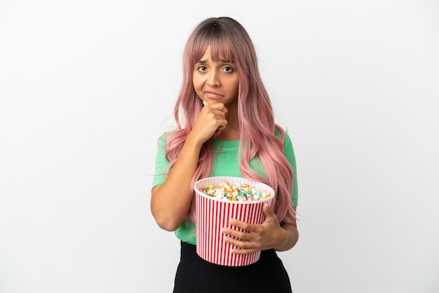 Young mixed race woman with pink hair eating popcorn isolated on white background thinking