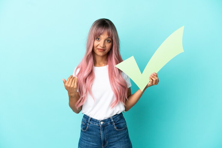 Photo young mixed race woman with pink hair isolated on blue background holding a check icon and doing coming gesture