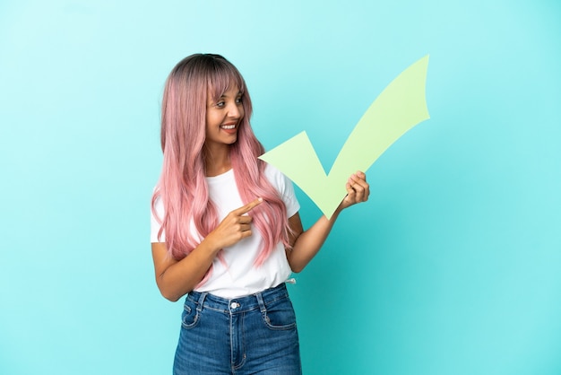 Young mixed race woman with pink hair isolated on blue background holding a check icon and pointing it