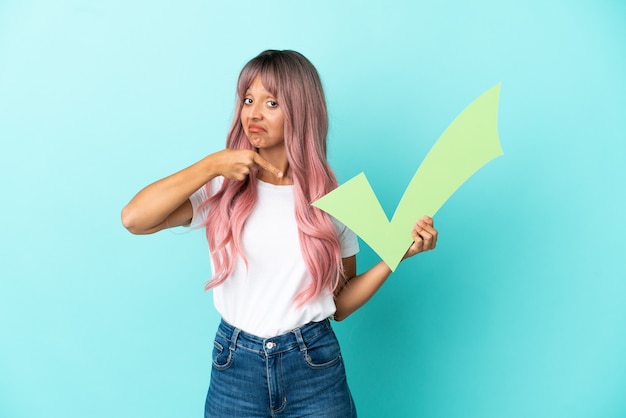 Young mixed race woman with pink hair isolated on blue background holding a check icon and pointing it