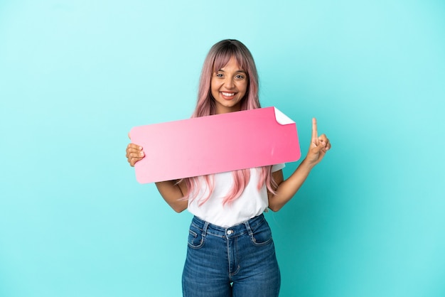 Young mixed race woman with pink hair isolated on blue background holding an empty placard