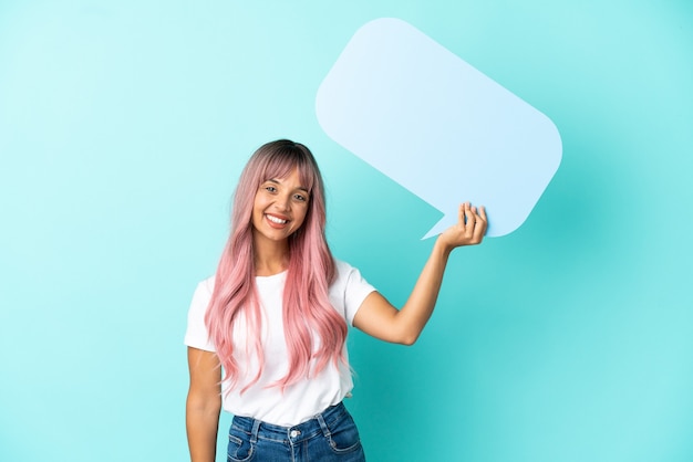 Young mixed race woman with pink hair isolated on blue background holding an empty speech bubble