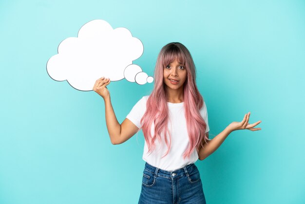 Foto giovane donna di razza mista con capelli rosa isolata su sfondo blu con in mano un fumetto pensante e con espressione triste