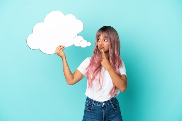 Young mixed race woman with pink hair isolated on blue background holding a thinking speech bubble