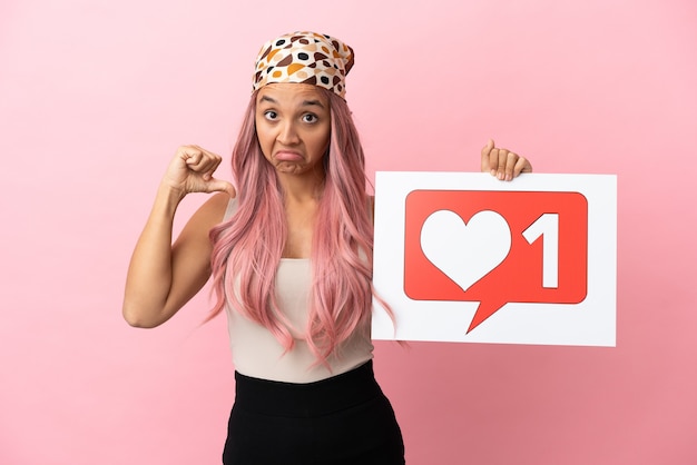 Молодая женщина смешанной расы с розовыми волосами, изолированная на розовом фоне, с гордым жестом держит плакат со значком Like