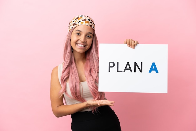 Young mixed race woman with pink hair isolated on pink background holding a placard with the message PLAN A and  pointing it