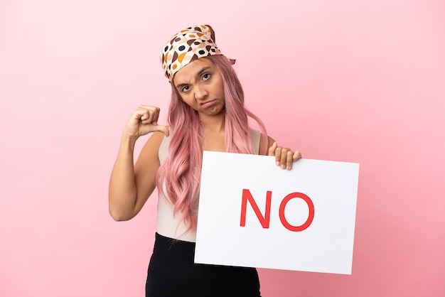 Foto giovane donna di razza mista con i capelli rosa isolata su sfondo rosa che tiene un cartello con il testo no