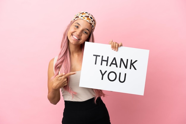 Photo young mixed race woman with pink hair isolated on pink background holding a placard with text thank you and  pointing it
