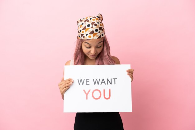 Photo young mixed race woman with pink hair isolated on pink background holding we want you board