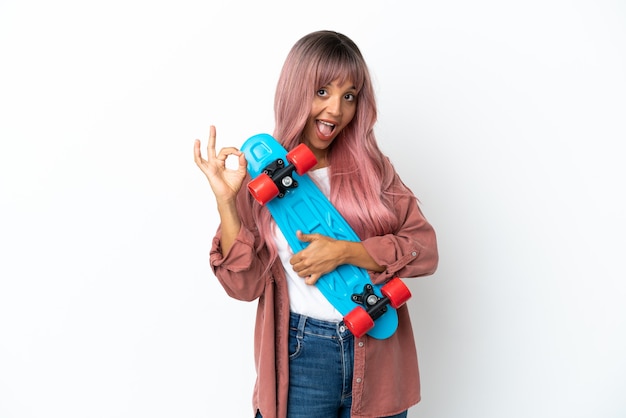 Young mixed race woman with pink hair isolated on white background with a skate and doing OK sign