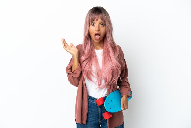 Young mixed race woman with pink hair isolated on white background with a skate and doing surprise gesture