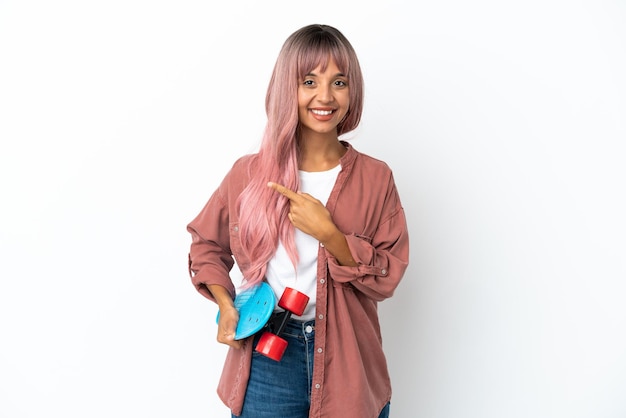 Young mixed race woman with pink hair isolated on white background with a skate and pointing to the side