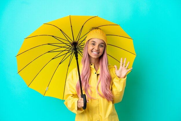 Young mixed race woman with rainproof coat and umbrella counting five with fingers