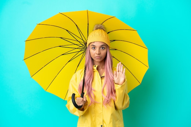 방수 코트와 우산을 들고 정지 제스처를 취하는 젊은 혼혈 여성