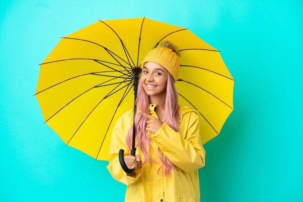 Young mixed race woman with rainproof coat and umbrella pointing to the side to present a product