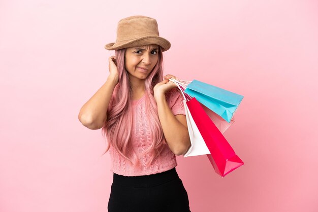 Young mixed race woman with shopping bag isolated on pink background having doubts