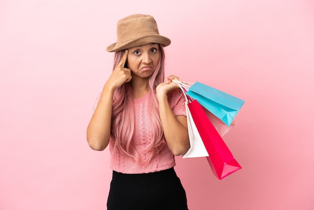 Young mixed race woman with shopping bag isolated on pink background thinking an idea