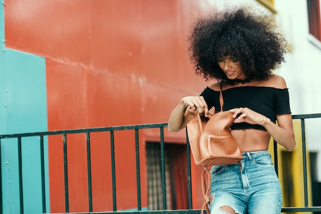 Young mixed woman looking for something in her bag