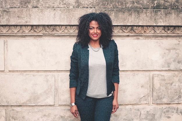 Young mixed woman with afro hairstyle smiling in urban background. Black girl wearing casual clothes. 