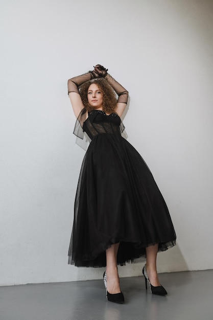 Young model in a black dress posing on a white wall