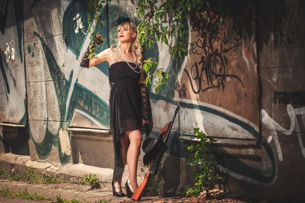 Young model in black dress standing near stone wall with graffiti