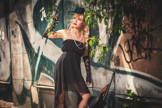 Young model standing in front of stone wall with graffiti near gun