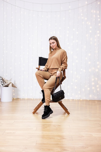 Young model woman in knitted suit, beige leather boots and sweater posing indoors