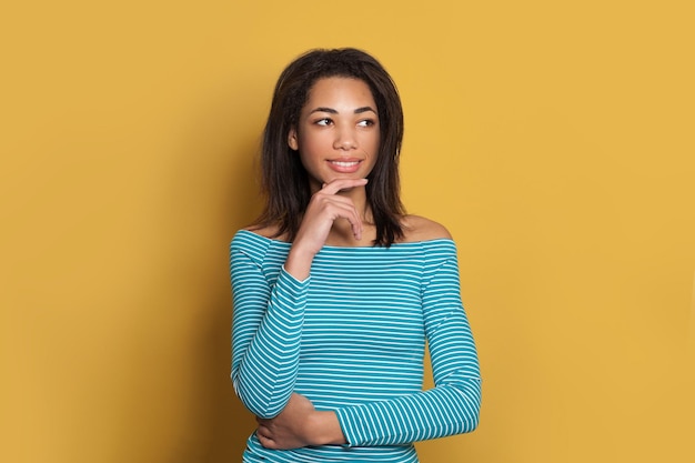 Young model woman thinking and smiling on colorful yellow background