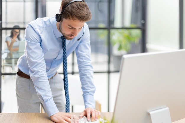 Giovane uomo d'affari moderno che analizza i dati utilizzando il computer mentre si lavora in ufficio con i colleghi sullo sfondo